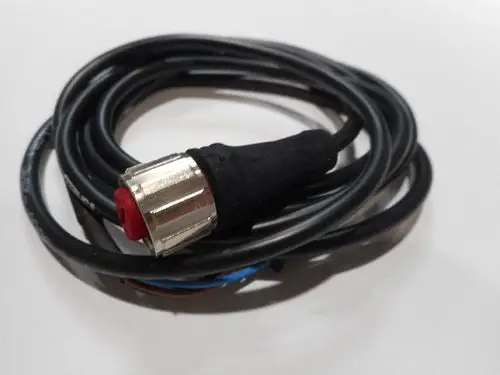 Schwarzes Kabel mit einer angeschlossenen Metallkupplung und rotem Kunststoffelement, möglicherweise für einen Durchflusssensor von Remeha.